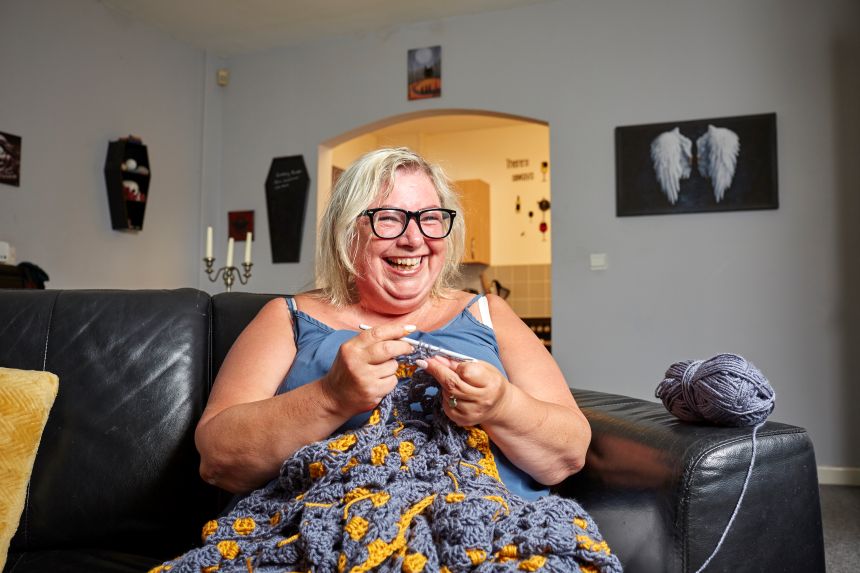 Anita smiling, crocheting on the sofa
