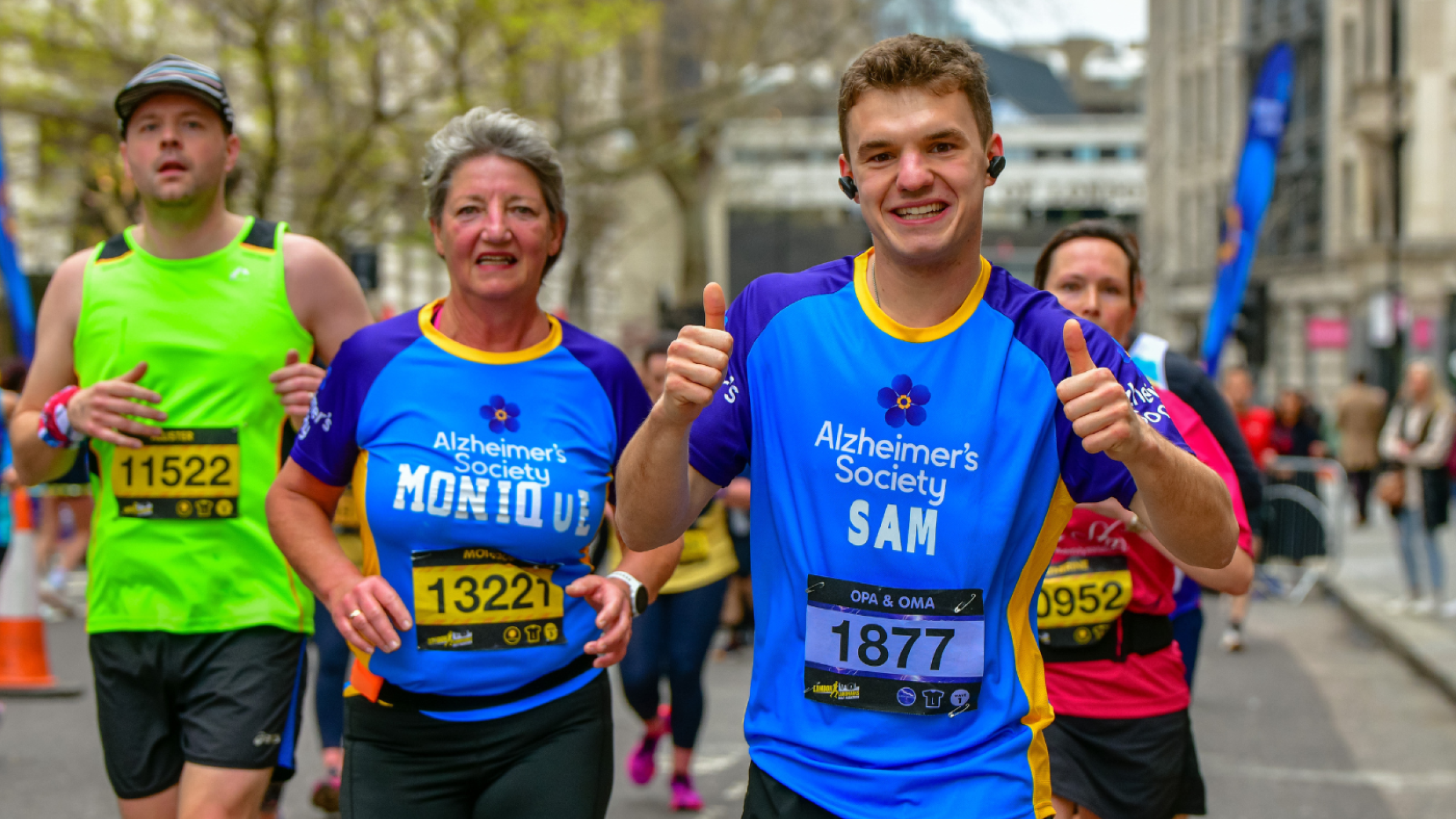 Two Alzheimer's Society runners competing, both smiling and one is giving two thumbs up