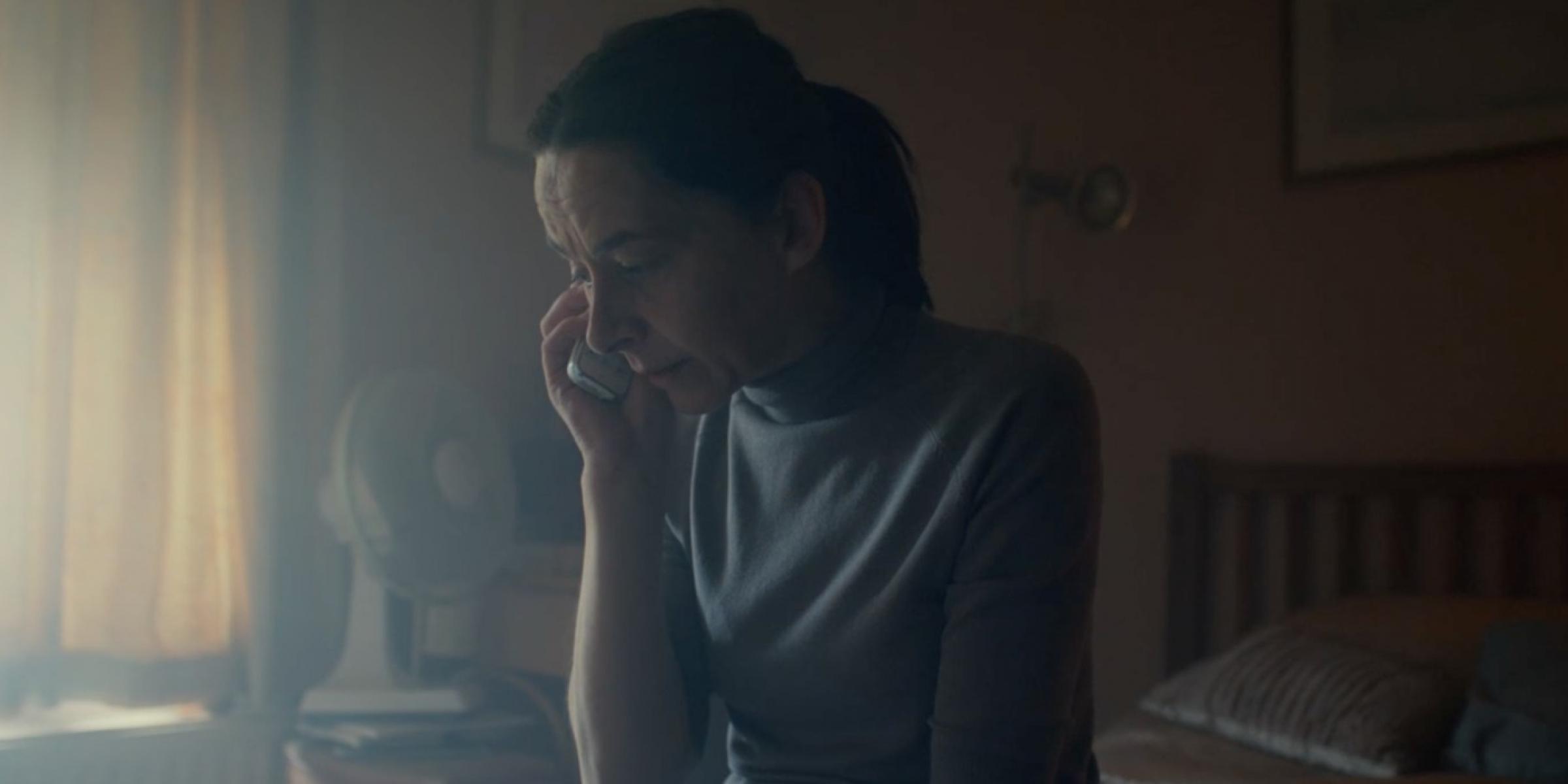 A woman is sitting in a dark room by herself talking on the phone
