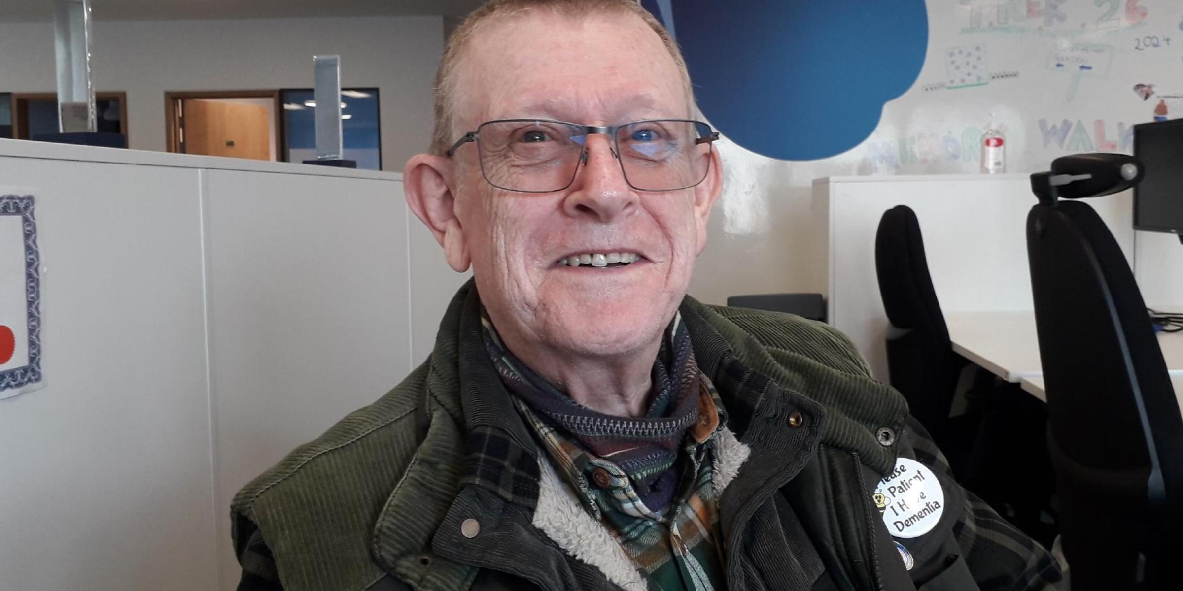 An almost bald man with glasses sat in an office, smiling