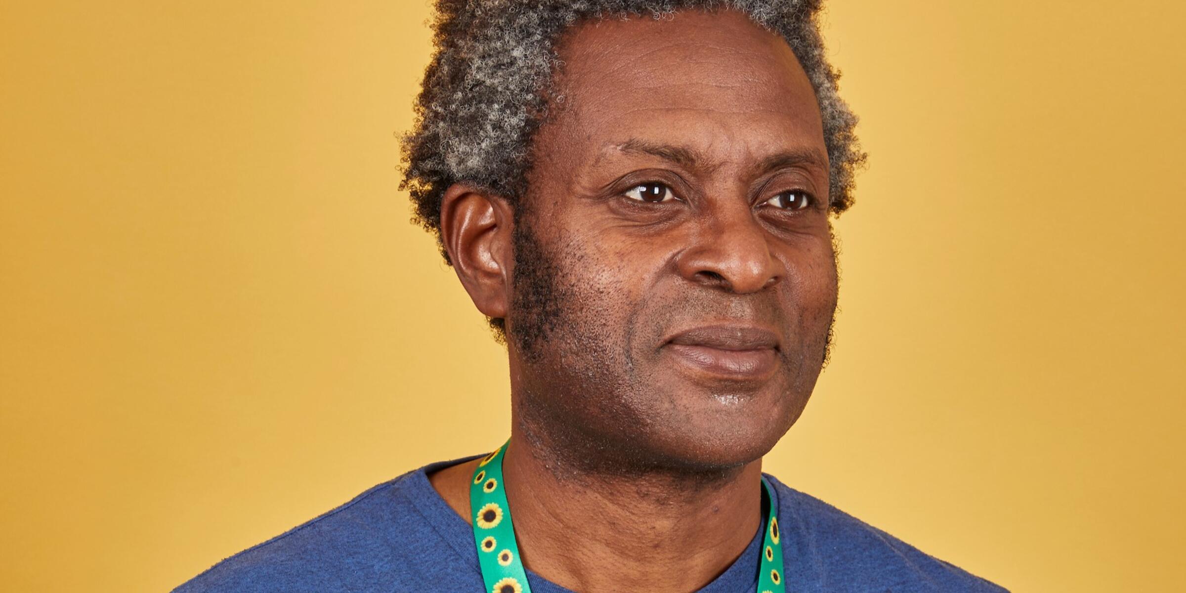 Man with grey and black curly hair wearing a blue t shirt and a sunflower lanyard