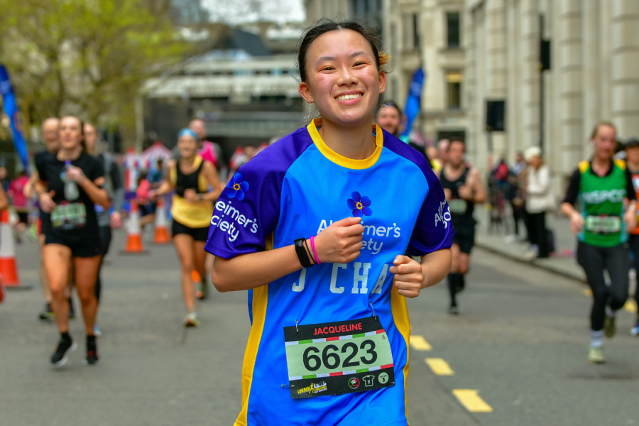 A person running ahead of a group down a city street, wearing an Alzheimers top, smiling at the camera.