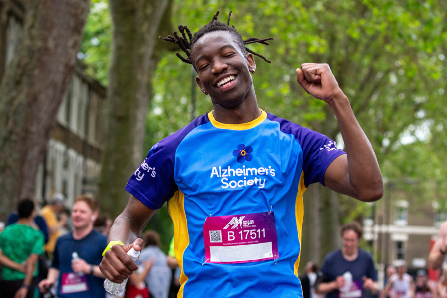 A gentleman punching the air with a mix of relief and tiredness on his face, with crowds around. He is dark skinned and wearing an Alzheimer's Society t-shirt and race number.