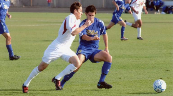 Two football players on a field running after a ball