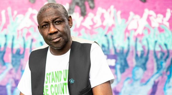 Ronald Amanze stands in front of wall of graffiti