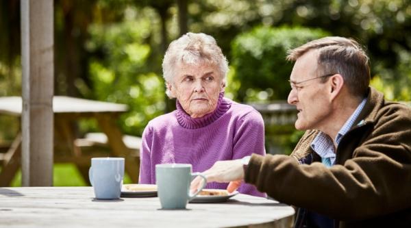 An older woman and man sitting at a table outside having a cup of tea
