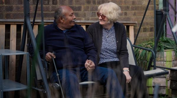 Ananga and Jo sit on a swingchair holding hands and looking each other