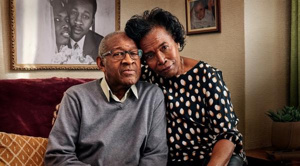 A wife with her arm around her husband at home