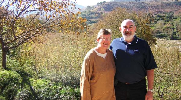 Ian and his wife stand in front of an open field in the sunshine