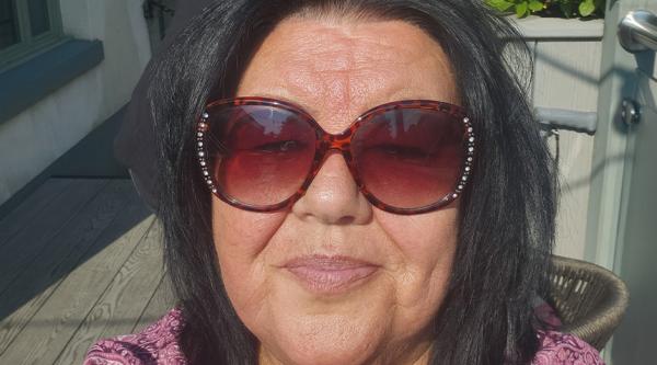 Carol Rimmer sat in sunshine wearing sunglasses and pink top