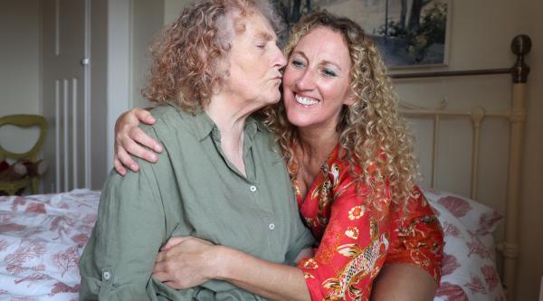 Sue giving Helen a kiss on the cheek in a bedrom