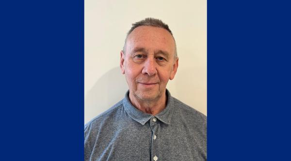 Martin is wearing a blue shirt and stood in front of a plain wall