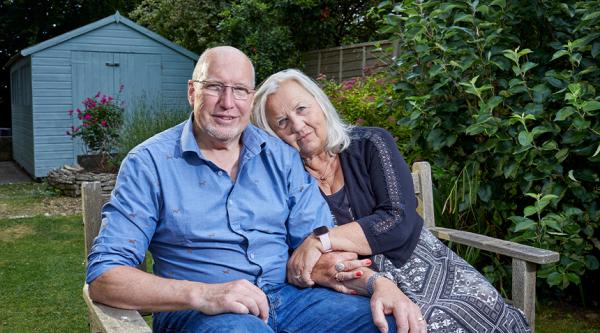 Martyn and Sarah hugging sat on a garden bench with a blue shed behind them