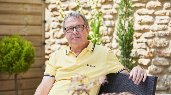 A man in a yellow shirt and glasses sits down in a garden