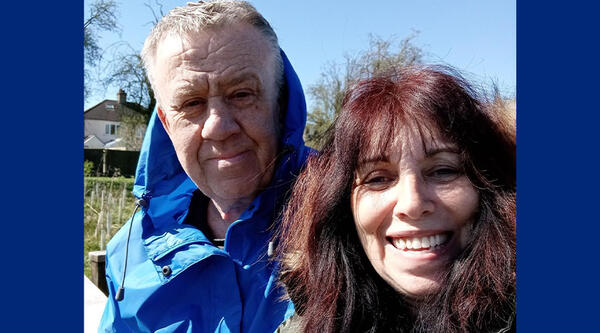 Man with white hair wearing a blue cagoule, woman to his right with brown hair smiling