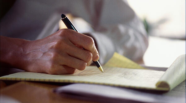Hand holding a pen, writing on a notepad
