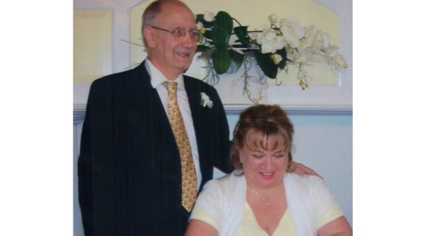 A man in a dark suit, yellow tie, white shirt and glasses, and a woman with auburn hair in an updo and yellow dress