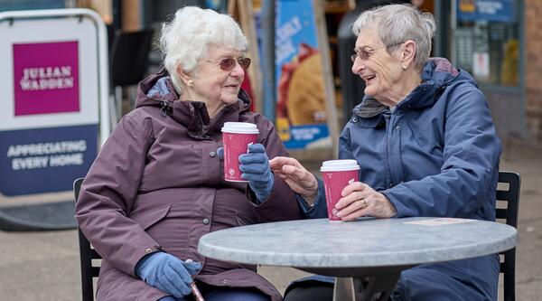 Two women drinking coffee outside sat around a table