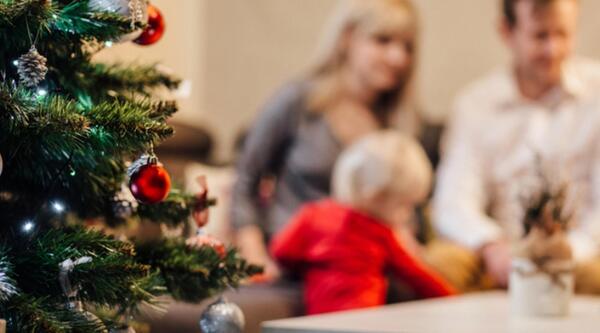 A close-up of a Christmas tree with parents and a toddler in the background
