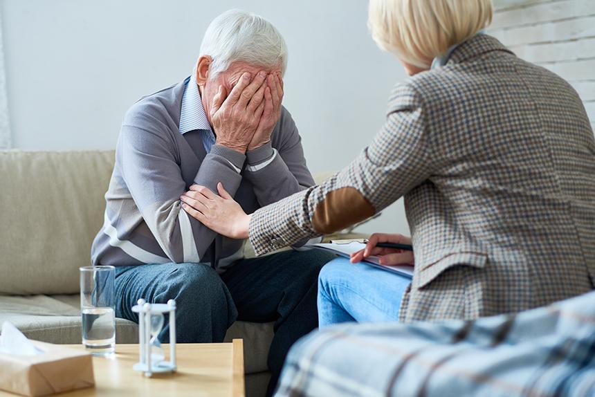 A man holding his head in his hands and being comforted by a woman sitting opposite him