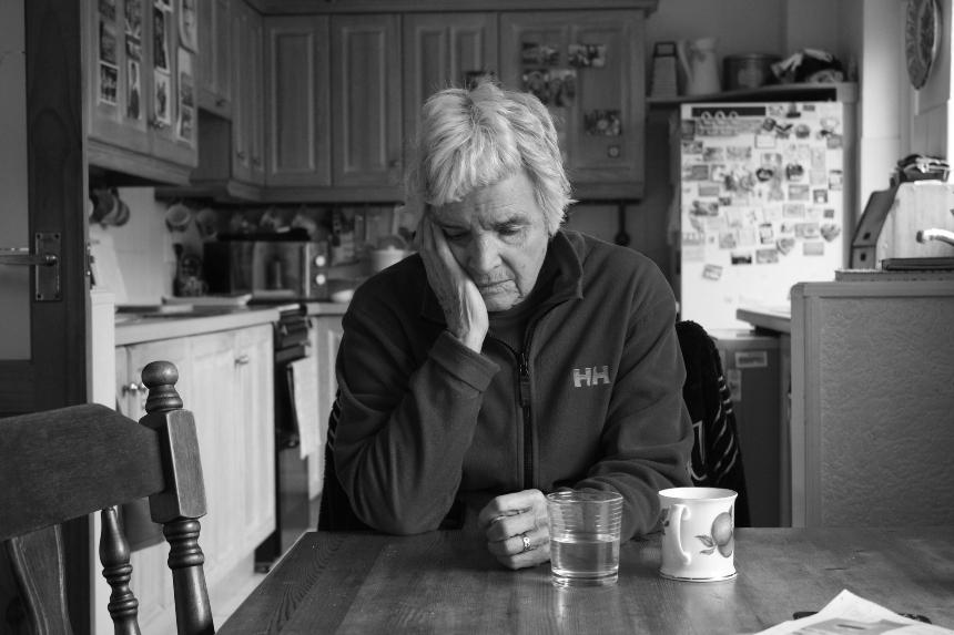Kyra's grandma, Winifred, sitting at a dining table, with her head resting on her hand looking into space