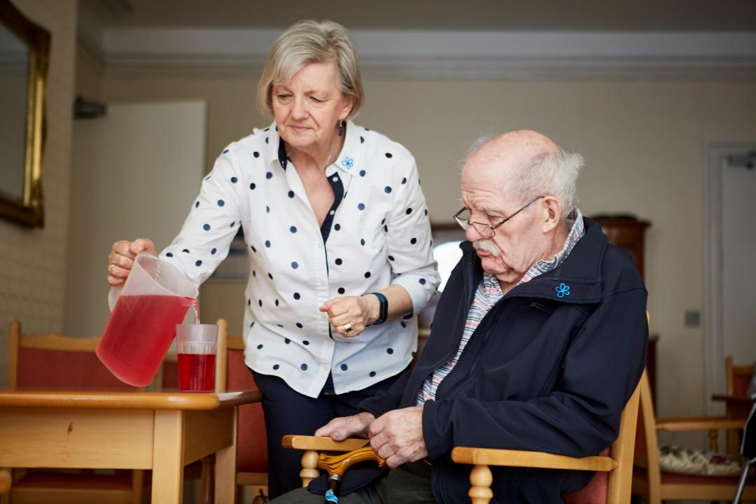 A woman pours juice into a cup for a man with dementia