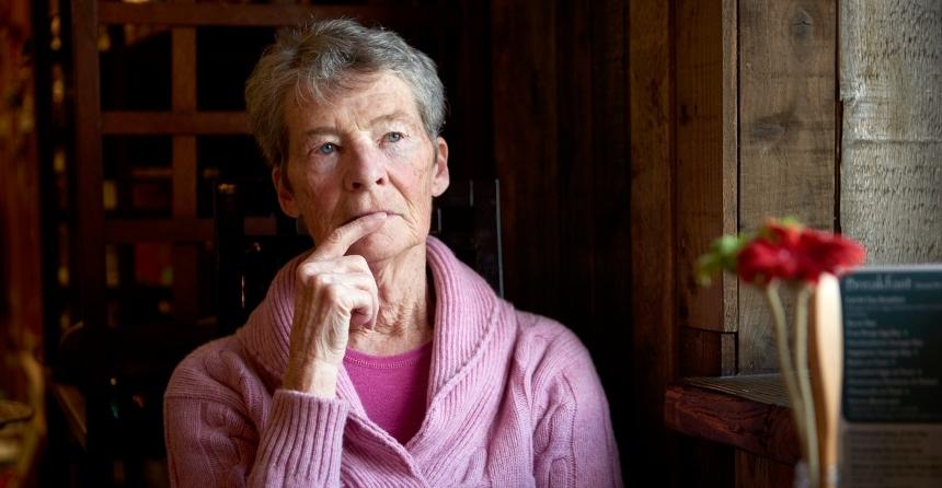 A woman sits in a dark room, looking thoughtful