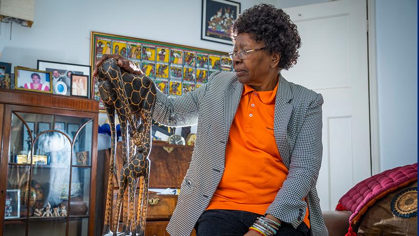 Nellie Suffolk sits next to a large giraffe figurine in her living room