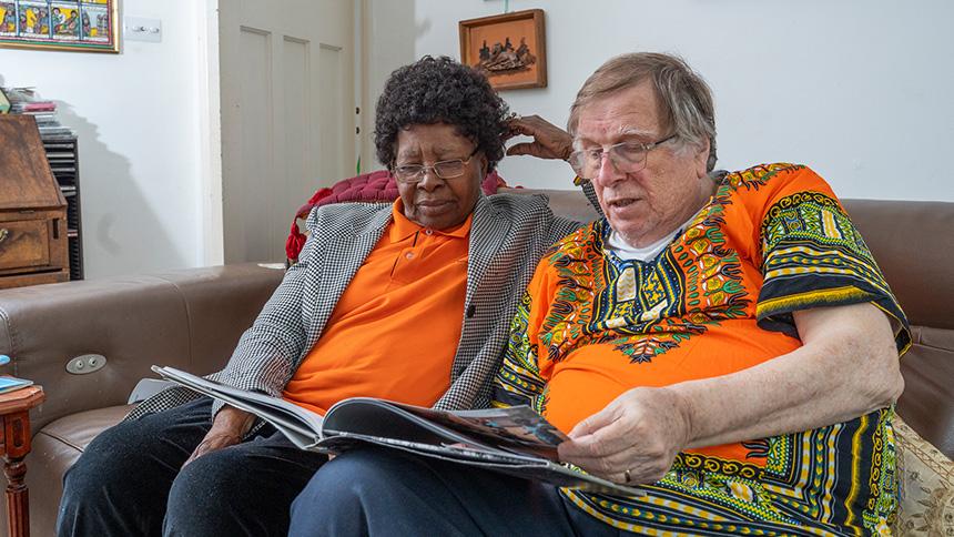 Nellie Suffolk sits with her husband John in their living room. They are looking through a photon album of old photos.