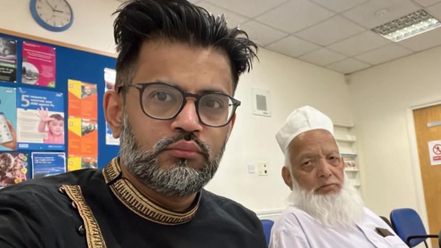 Shahbaz and Muhammad sit next to each other. Shahbaz is dressed in black and his father is wearing white.