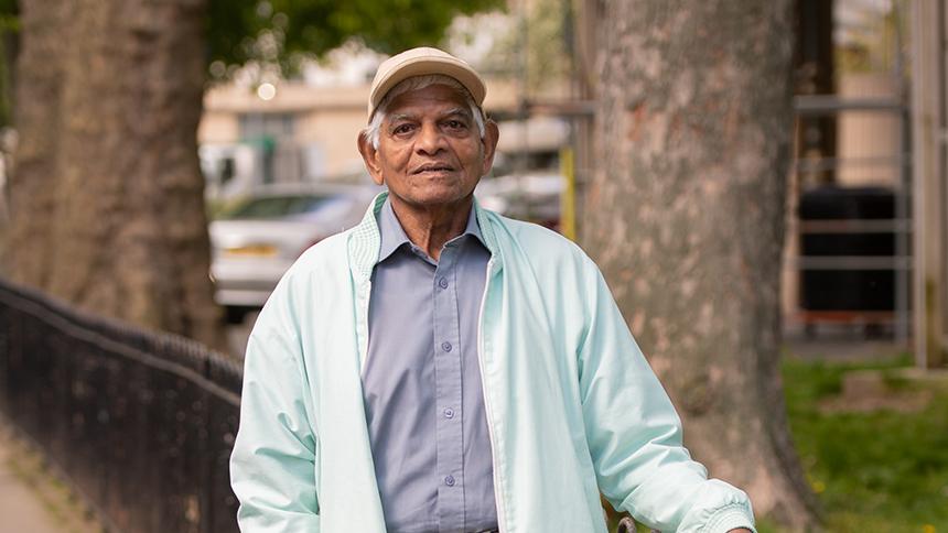 Lal Kissoon stands outside, he's looking at the camera wearing a baseball cap, blue shirt and bomber jacket.
