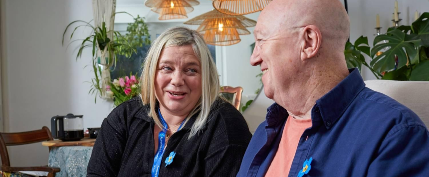 A woman with an Alzheimer's Society lanyard talks to a smiling man.