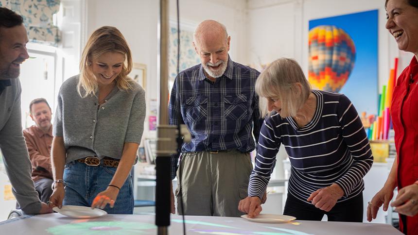 Carers and people with dementia stood up and looking a projected light game on a tabletop