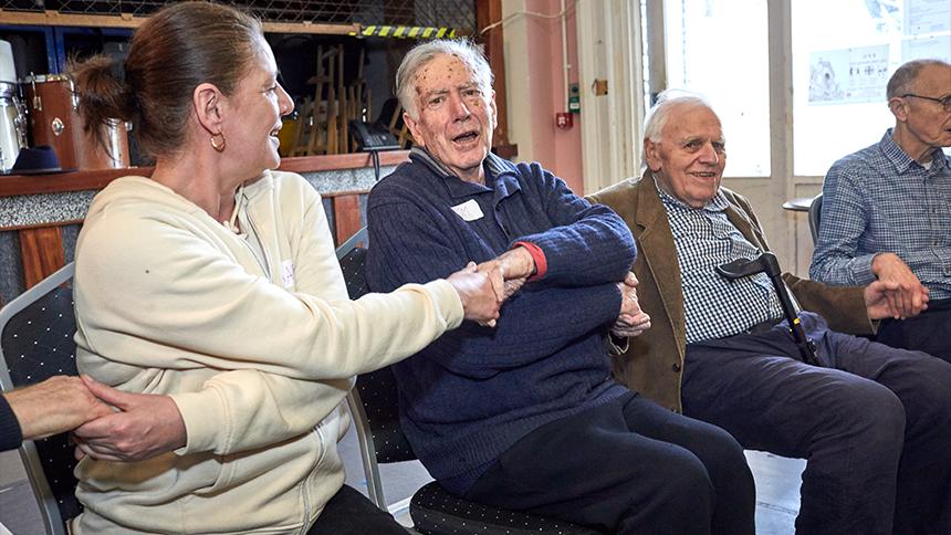 Row of people sat down and holding hands as they sing