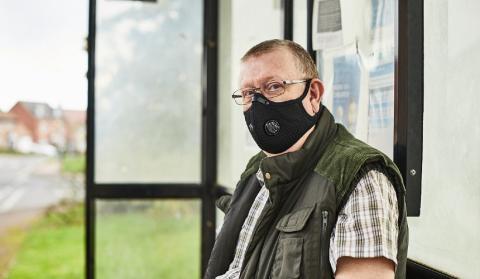 A man wearing a face covering at the bus stop
