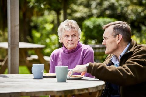 An older woman and man sitting at a table outside having a cup of tea