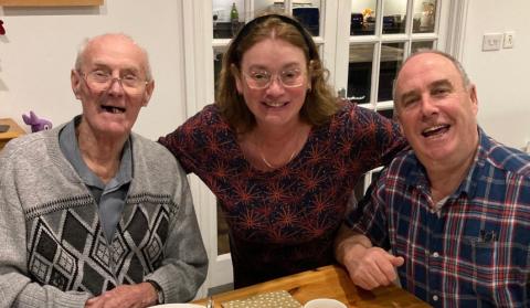 Irene between Rodger and Chris with her arms around them, all smiling together, at an afternoon tea