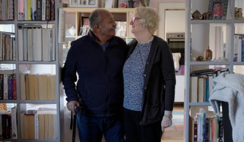 Ananga and Jo stand in a library, looking at each other and smiling