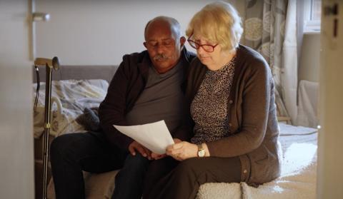 Ananga and Jo sit on the side of their bed, reading a piece of paper together