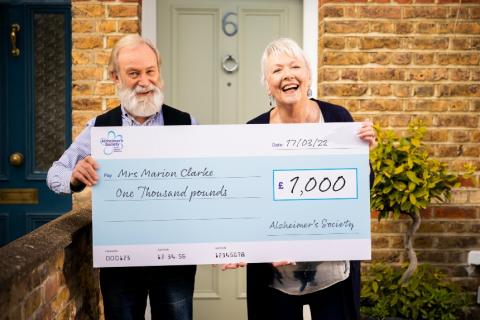 A couple smiling while holding a large cheque for £1000