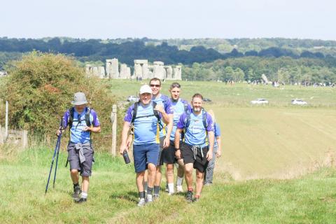 A group of 3 trekkers walking with Stonehenge in the background