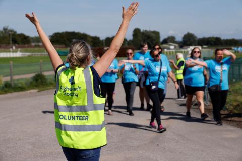 Volunteer in high vis with arms up, cheering at walkers waving