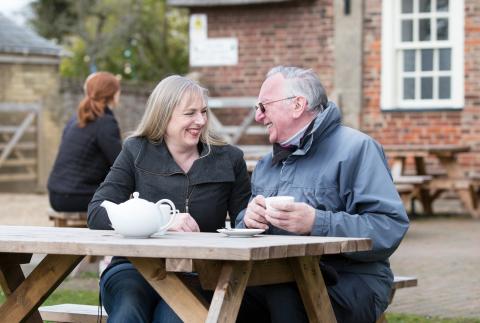 A couple on an outdoor restaurant bench smiling at each other 