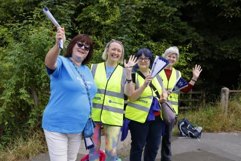 Four female volunteers smiling and waving at the camera with cheer materials.