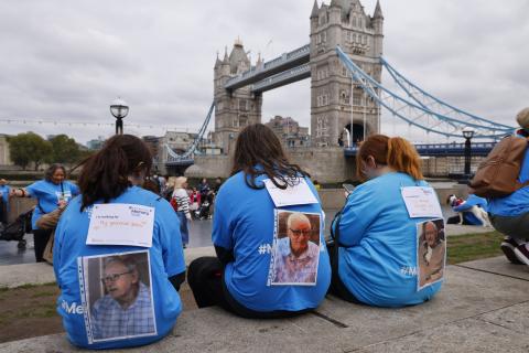 3 people in blue Memory Walk t-shirts, sitting in front of Tower Bridge in London, with pictures of loved ones and message on their backs.