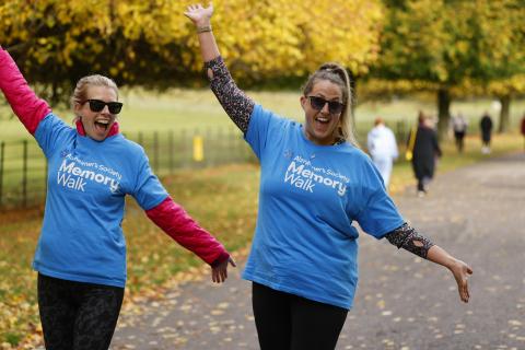 2 women in blue Memory Walk t-shirts, smiling at the camera with their hands in the air.