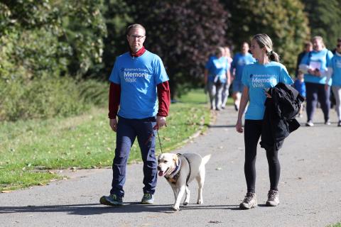 Two people in blue Memory Walk t-shirts, walking with a dog.