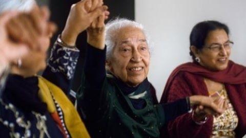 Three women in saris sit together, holding raised hands
