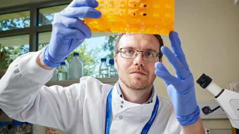 A male researcher holds up laboratory equipment.