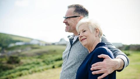 A man and woman stand embracing on a sunny hill.